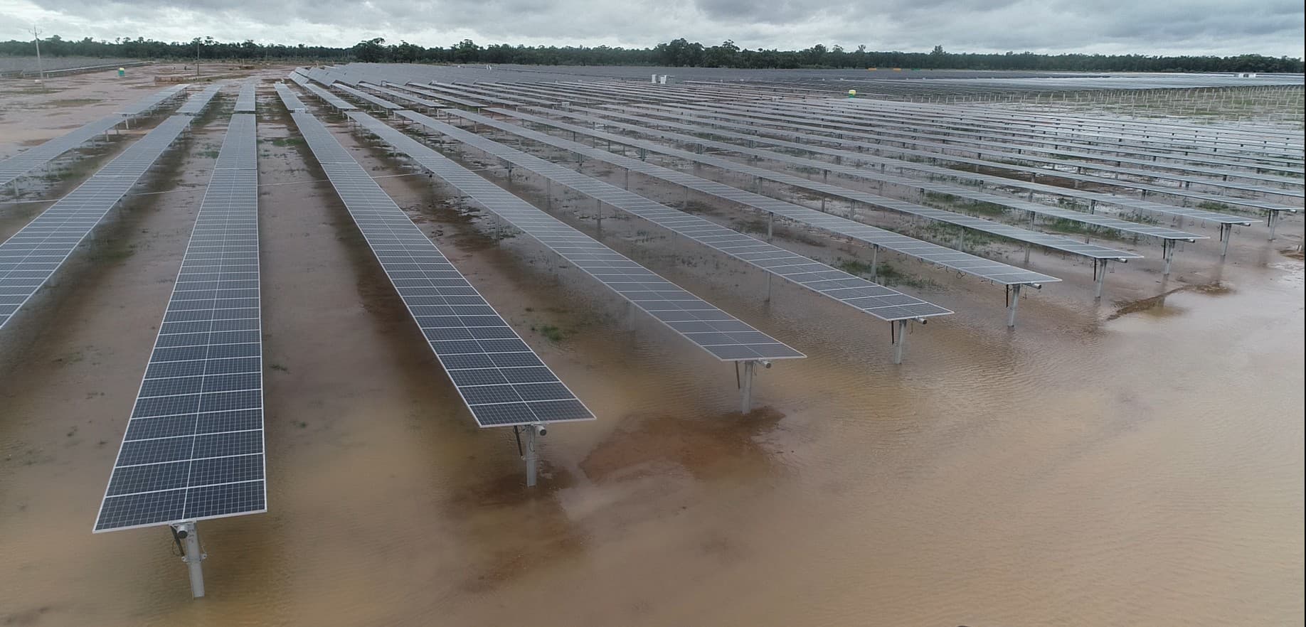 Rows of solar panels standing in deep, muddy floodwaters under a grey, overcast sky.